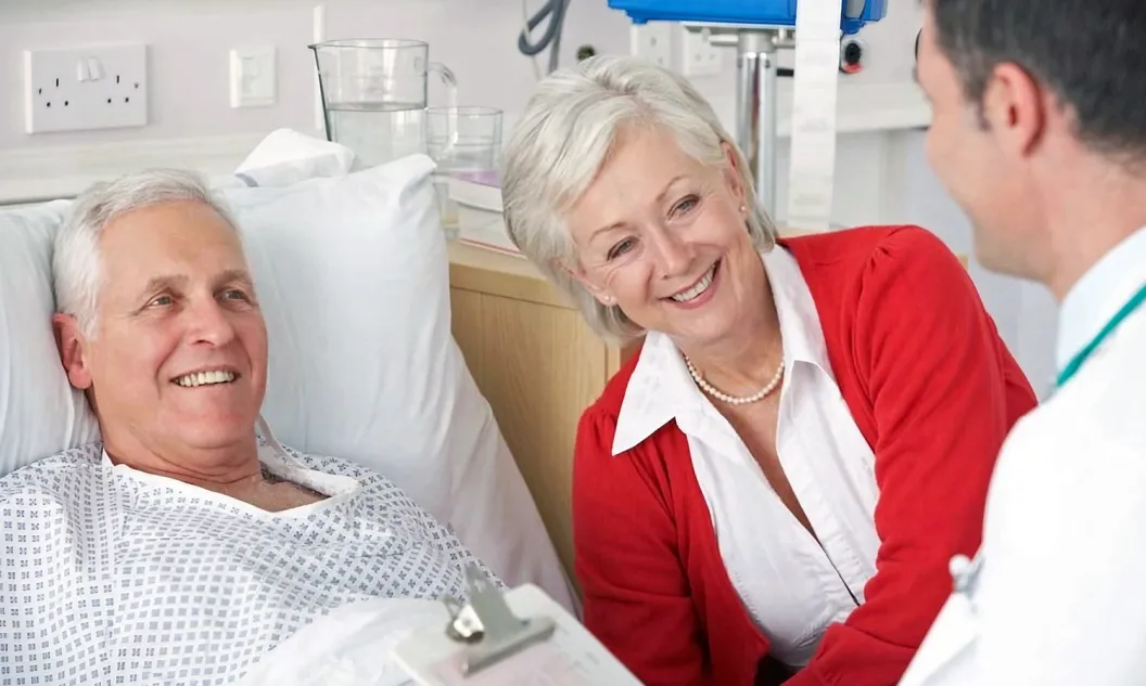Doctor talking to man in hospital bed with his wife alongside